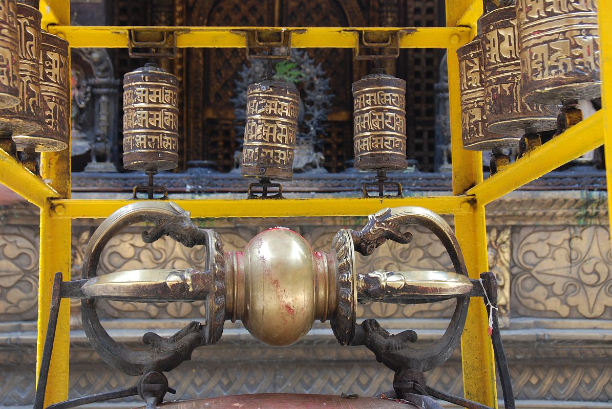 Kathmandu Patan Golden Temple 08 Vajra And Prayer Wheels An enormous vajra is flanked by prayer wheels just inside the entrance to Golden Temple in Patan. The Swaymbhu Chaitya is behind.
